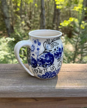 Load image into Gallery viewer, White mug with blue cosmic and floral design on a wooden surface with a forest background