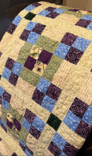 Load image into Gallery viewer, A handmade patchwork quilt draped over a chair, featuring a mix of blue, purple, green, and beige patterned fabric squares.
